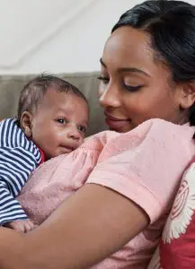 Mother lovingly holds her baby close on a couch.