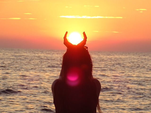 Silhouette of a person holding the sun like horns at sunset over the ocean.